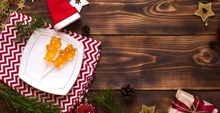 Two lollipops on stick in shape of symbol new year 2021 - bull on white saucer, towel with ornaments and Christmas decor on wooden background. Jewelry stars, beads, ball, fir. Flat lay, copy spaceの写真素材