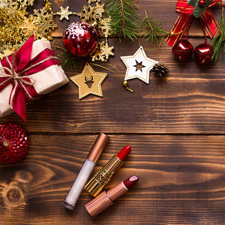 Red lipstick and lip gloss and eyelids on a wooden background in the Christmas decor. Holiday makeup for the new year, gift, shopping, women's desires. Space for text, flat layの写真素材