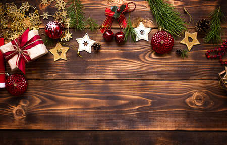 Frame with Christmas decor on a wooden background. New year, holiday atmosphere, green spruce branches, decorations: stars, gift box, beads, ball, bells, cones. Space for text, flat layの写真素材