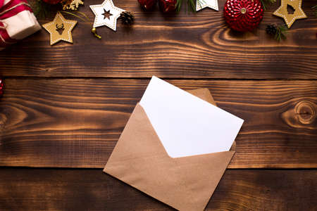 Mail envelope made of craft paper with a white sheet for text on a wooden background with Christmas decor. A letter to Santa Claus, a wish list, a new year's dream, a gift. Flat lay, copy spaceの写真素材