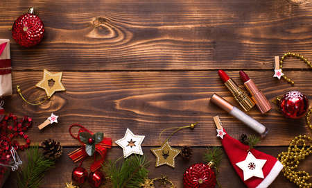 Red lipstick and lip gloss and eyelids on a wooden background in the Christmas decor. Holiday makeup for the new year, gift, shopping, women's desires. Space for text, flat layの写真素材