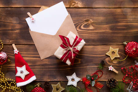 Mail envelope made of craft paper with a white sheet for text on a wooden background with Christmas decor. A letter to Santa Claus, a wish list, a new year's dream, a gift. Flat lay, copy spaceの写真素材