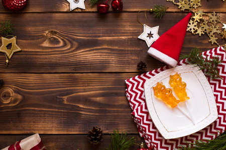 Two lollipops on stick in shape of symbol new year 2021 - bull on white saucer, towel with ornaments and Christmas decor on wooden background. Jewelry stars, beads, ball, fir. Flat lay, copy spaceの写真素材