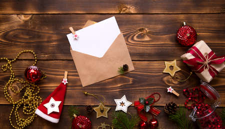 Mail envelope made of craft paper with a white sheet for text on a wooden background with Christmas decor. A letter to Santa Claus, a wish list, a new year's dream, a gift. Flat lay, copy spaceの写真素材