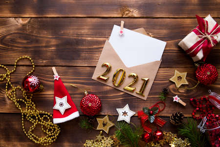 Mail envelope of craft paper with white sheet for text on wooden background with Christmas decor and Golden numbers 2021. letter to Santa Claus, wish list, new year's dream, gift. Flat lay, copyspaceの写真素材