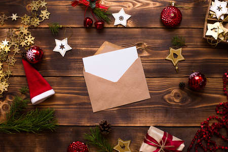 Mail envelope made of craft paper with a white sheet for text on a wooden background with Christmas decor. A letter to Santa Claus, a wish list, a new year's dream, a gift. Flat lay, copy spaceの写真素材
