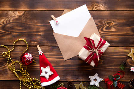 Mail envelope made of craft paper with a white sheet for text on a wooden background with Christmas decor. A letter to Santa Claus, a wish list, a new year's dream, a gift. Flat lay, copy spaceの写真素材