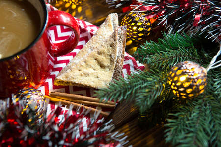 Triangular cookies with powdered sugar and cinnamon on a napkin with a zigzag pattern in the Christmas decor. Red coffee mug with marshmallow, spruce branches, garland, new year, comfort.の写真素材