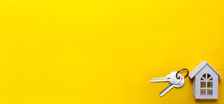 White wooden house symbol and keys on a yellow background. Cottage construction concept, layout and design, architectural plan, moving to a new house, realtor Agency. Space for text, flatlyの写真素材