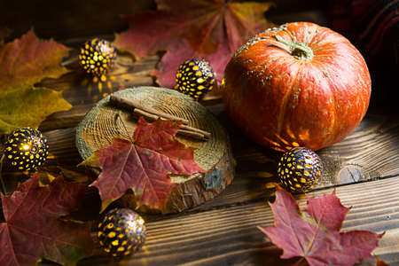 Orange natural round pumpkin on a wooden table with fallen yellow and red maple leaves, cinnamon sticks. Lights garlands, warm autumn atmosphere, thanksgiving, harvest festival, Halloween. Copy spaceの写真素材
