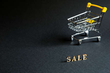Shopping cart and the inscription "Sale" on a black background. Black Friday, discounts, sale, shopping, interest sign. Space for textの写真素材