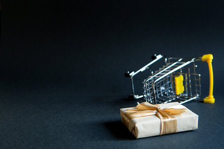 Box with a gift in Christmas packaging in a shopping cart on a black background. Black Friday,...