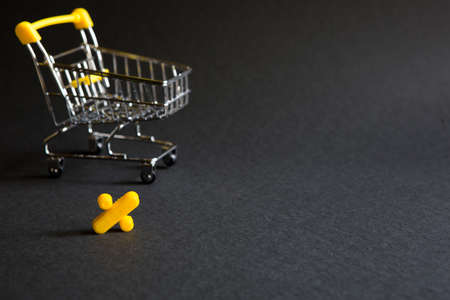 Yellow plastic sign percent on a black background with the shopping cart. Black Friday, discount percentage, shopping, buying and selling, promotion. Space for textの写真素材