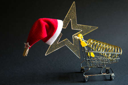 Shopping cart with a gold transparent star with sequins in the shape of a Christmas tree on a black background. Black Friday, buying gifts for the new year. Space for textの写真素材