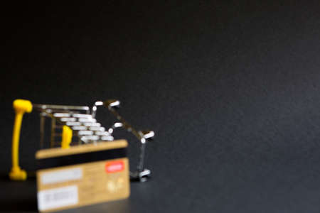 Defocus empty grocery cart from a supermarket and plastic gold credit Bank card on black background. Black Friday, shopping cart, shopping, online store, sale, discounts. Space for text. Blurredの写真素材