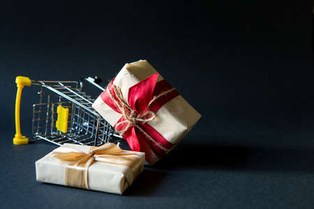 Box with a gift in Christmas packaging in a shopping cart on a black background. Black Friday, buying gifts for the new year. Space for textの写真素材