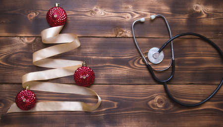 Christmas flat lay on a medical theme. Decorations for the new year from stars, ball, ribbons, Santa hats, and a doctor's stethoscope. Wooden background, space for textの写真素材