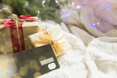Box with a gift in Christmas packaging in shopping cart on white knitted blanket. Black Friday, buying gifts for new year. Holiday decor, Bank plastic card - cashless payment, online store. Copy spaceの写真素材
