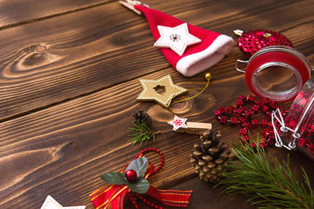 Christmas decorations on a wooden background. Beads in a glass jar with a lid, stars, Santa hat, cones, pine branches. New year, preparation for the holiday. Space for textの写真素材