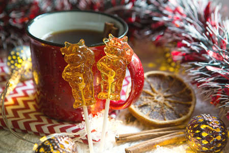 Two lollipops on stick in shape of symbol new year 2021 - bull on the background Christmas decor with a red Cup of tea. Garlands, cinnamon and dried orange - atmosphere of warmth, comfort and magic.の写真素材