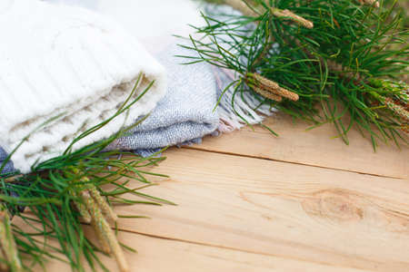 Christmas flatlay on a rustic wooden background: green pine needles with cones, warm woolen things in white and blue. New year's concept, winter holiday home comfort. Space for textの写真素材
