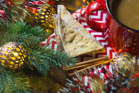 Triangular cookies with powdered sugar and cinnamon on a napkin with a zigzag pattern in the Christmas decor. Red coffee mug with marshmallow, spruce branches, garland, new year, comfort.の写真素材