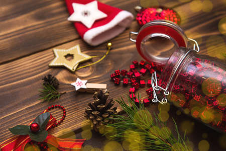 Christmas decorations on a wooden background. Beads in a glass jar with a lid, stars, Santa hat, cones, pine branches. New year, preparation for the holiday. Space for textの写真素材