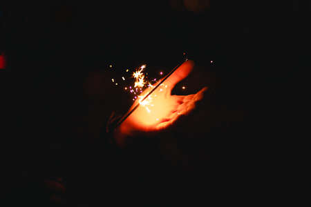 Sparks and light from sparklers in the dark on the palm of a person. Christmas magic, new year's eve, festive background. Space for textの写真素材