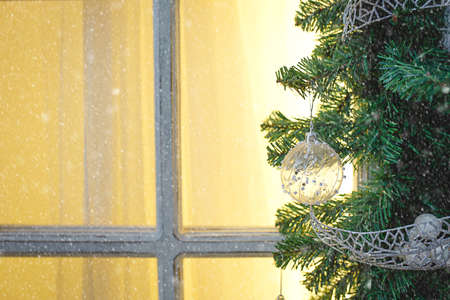 Christmas decorations made of spruce branches and white transparent balls and ribbons frame the window with wooden frame and yellow light. New year festive atmosphere, comfort of home. Space for textの写真素材