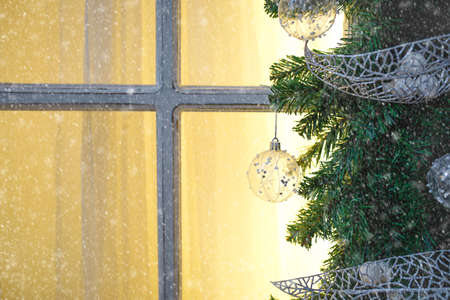 Christmas decorations made of spruce branches and white transparent balls and ribbons frame the window with wooden frame and yellow light. New year festive atmosphere, comfort of home. Space for textの写真素材