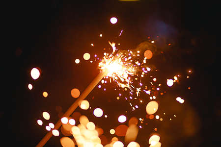 Sparks and light from sparklers in the dark with bright yellow and orange bokeh and smoke. Festive fire texture, background for new year and Christmas.の写真素材