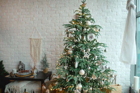 Christmas interior in the style of a Scandinavian loft: gray concrete, wooden decor, incandescent lamps, realistic artificial Christmas tree. Cozy new year in a country houseの写真素材