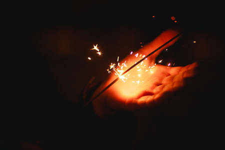 Sparks and light from sparklers in the dark on the palm of a person. Christmas magic, new year's eve, festive background. Space for textの写真素材