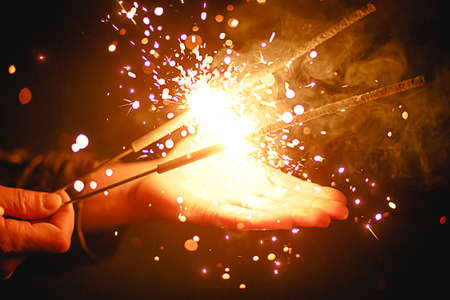 Sparks and light from sparklers in the dark on the palm of a person. Christmas magic, new year's eve, festive background. Space for textの写真素材