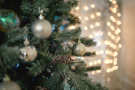 Silver Christmas decor on a green artificial fir tree with lights garlands in bokeh in the background. New year, Christmas toys, ball close-up. Space for text.の写真素材