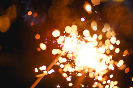 Sparks and light from sparklers in the dark with bright yellow and orange bokeh and smoke. Festive fire texture, background for new year and Christmas.の写真素材