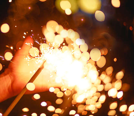 Sparks and light from sparklers in the dark on the palm of a person. Christmas magic, new year's eve, festive background. Space for textの写真素材