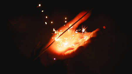 Sparks and light from sparklers in the dark on the palm of a person. Christmas magic, new year's eve, festive background. Space for textの写真素材