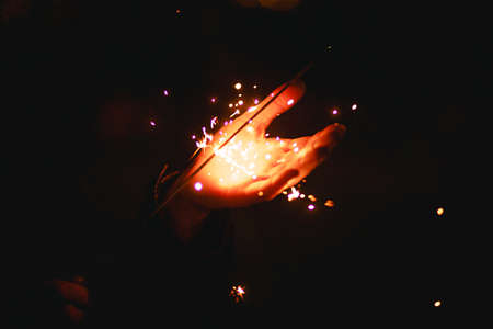Sparks and light from sparklers in the dark on the palm of a person. Christmas magic, new year's eve, festive background. Space for textの写真素材