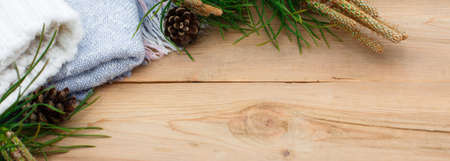 Christmas flatlay on a rustic wooden background: green pine needles with cones, warm woolen things in white and blue. New year's concept, winter holiday home comfort. Space for textの写真素材