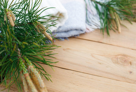 Christmas flatlay on a rustic wooden background: green pine needles with cones, warm woolen things...