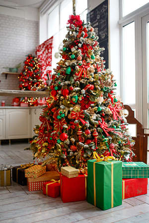 The Christmas tree is decorated with red and green toys, boxes with gifts on the floor. New year's atmosphere in the house, festive interior.の写真素材