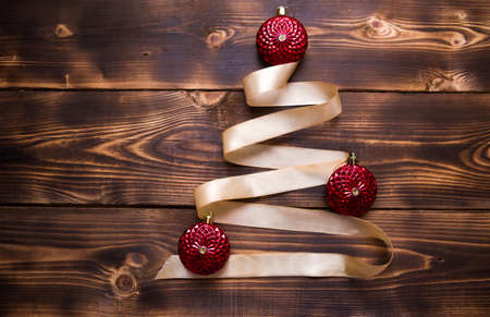 A Christmas tree made of gold ribbon decorated with red round toys on a dark wooden background. Flat lay. Space for text. New yearの写真素材