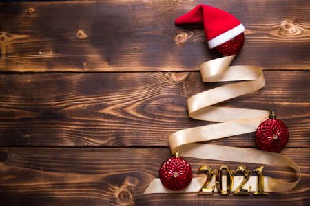 A Christmas tree made of gold ribbon with the numbers 2021 is decorated with red balloons on a dark wooden background. Flat lay. Space for text. New year, Santa hat.の写真素材