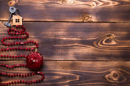 Key to the house with a keychain on top of Christmas tree made of red square beads. Flat lay on wooden background. Building or buying a house in new year. Mortgage, real estate rental. Space for textの写真素材