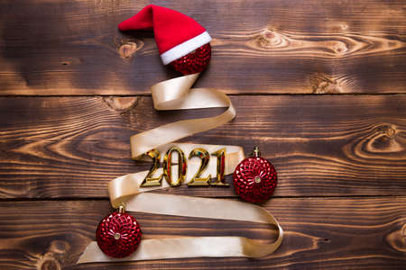 A Christmas tree made of gold ribbon with the numbers 2021 is decorated with red balloons on a dark wooden background. Flat lay. Space for text. New year, Santa hat.の写真素材