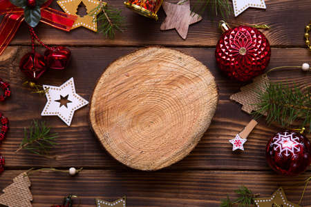Christmas flat lay of red balloons and wooden stars and clothespins on a dark background with tree trunk section for notes in center. New year's frame, space for text. Xmas toys, beads, pine branchesの写真素材