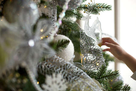 Transparent glass deer pendant on Christmas tree with lights garlands. White Christmas decor, feathers, balloons, flowers, ribbons. New year, the atmosphere of celebration and magic. Space for textの写真素材