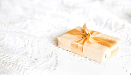 Box with Christmas gift in light paper is tied with a gold ribbon on white knitted background with decor. Golden garland of stars. New Year. Congratulations, surprise. space for textの写真素材