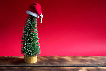 Christmas tree on a red background with lights of garlands, caramel striped cane, Santa hat, tinsel. New year, festive atmosphere. Copy spaceの写真素材